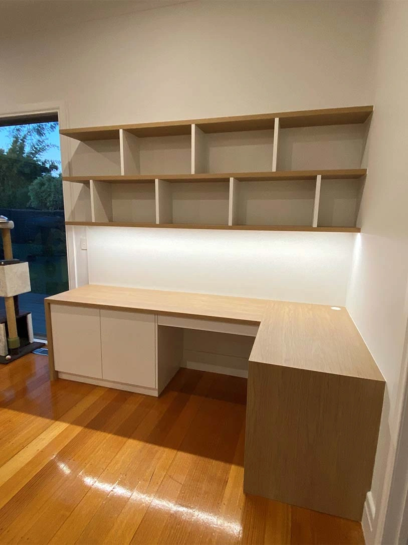 A desk with an integrated shelf, located next to a window