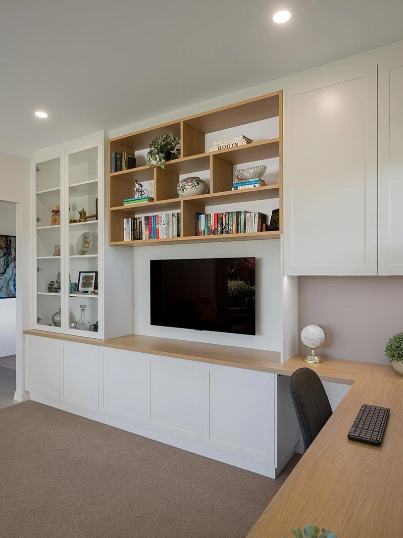 Well-organized home office featuring a desk, a bookshelf filled with books, and a television for entertainment