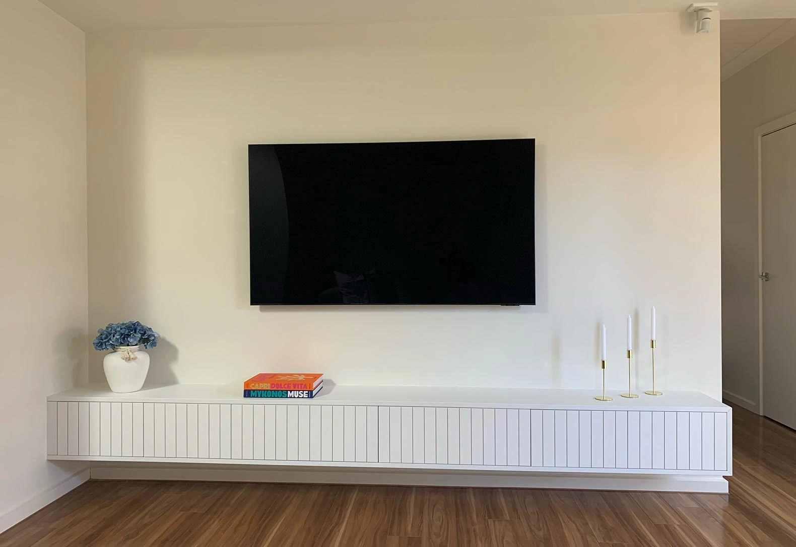 A modern white TV is fixed to the wall, overlooking a rich wooden floor, adding elegance to the room's design