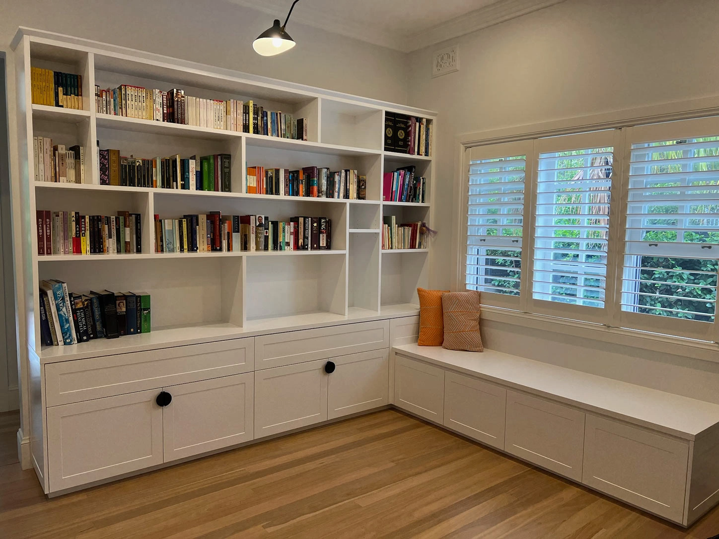 A white bookcase and a comfortable window seat under a large window, perfect for enjoying natural light while reading