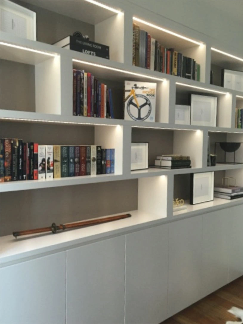 A white bookcase illuminated by soft lights, showcasing neatly arranged books and decorative items