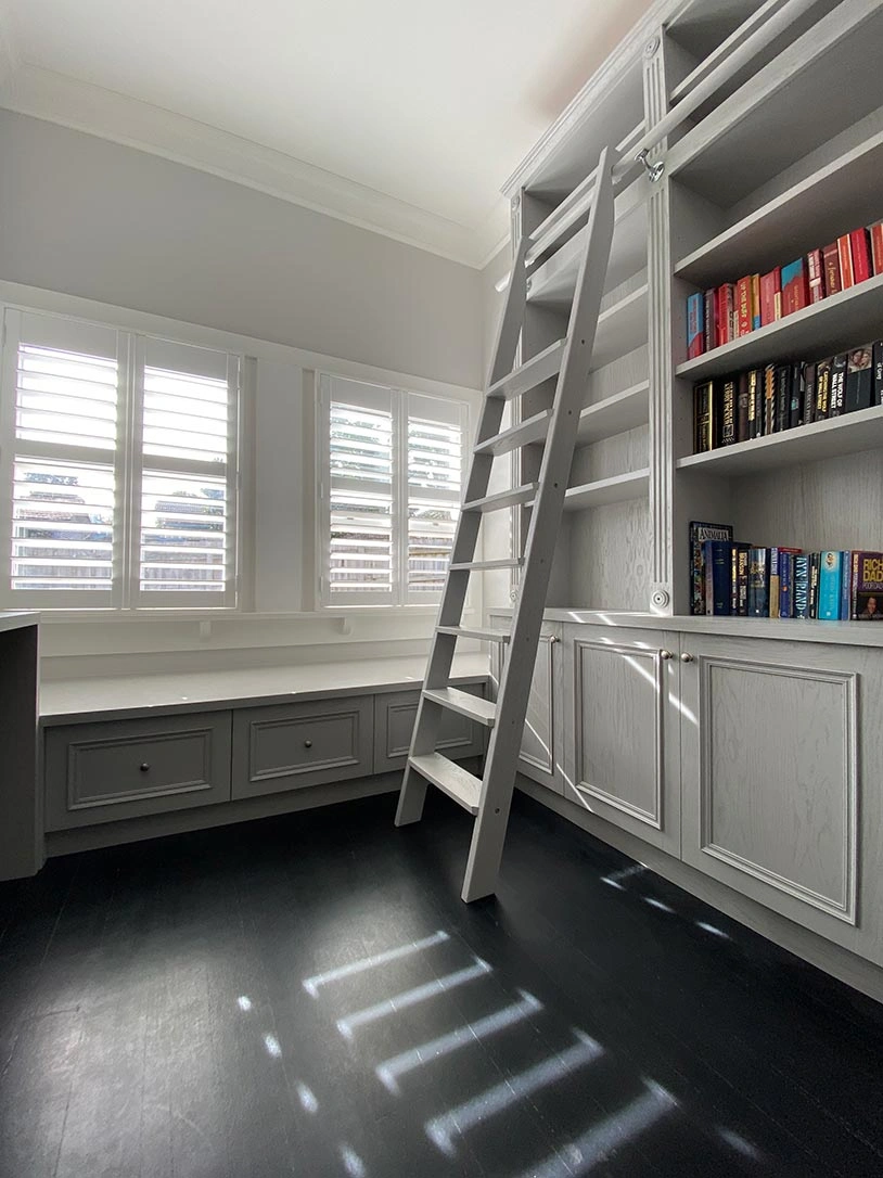 A bright room showcasing a ladder next to shelves overflowing with books