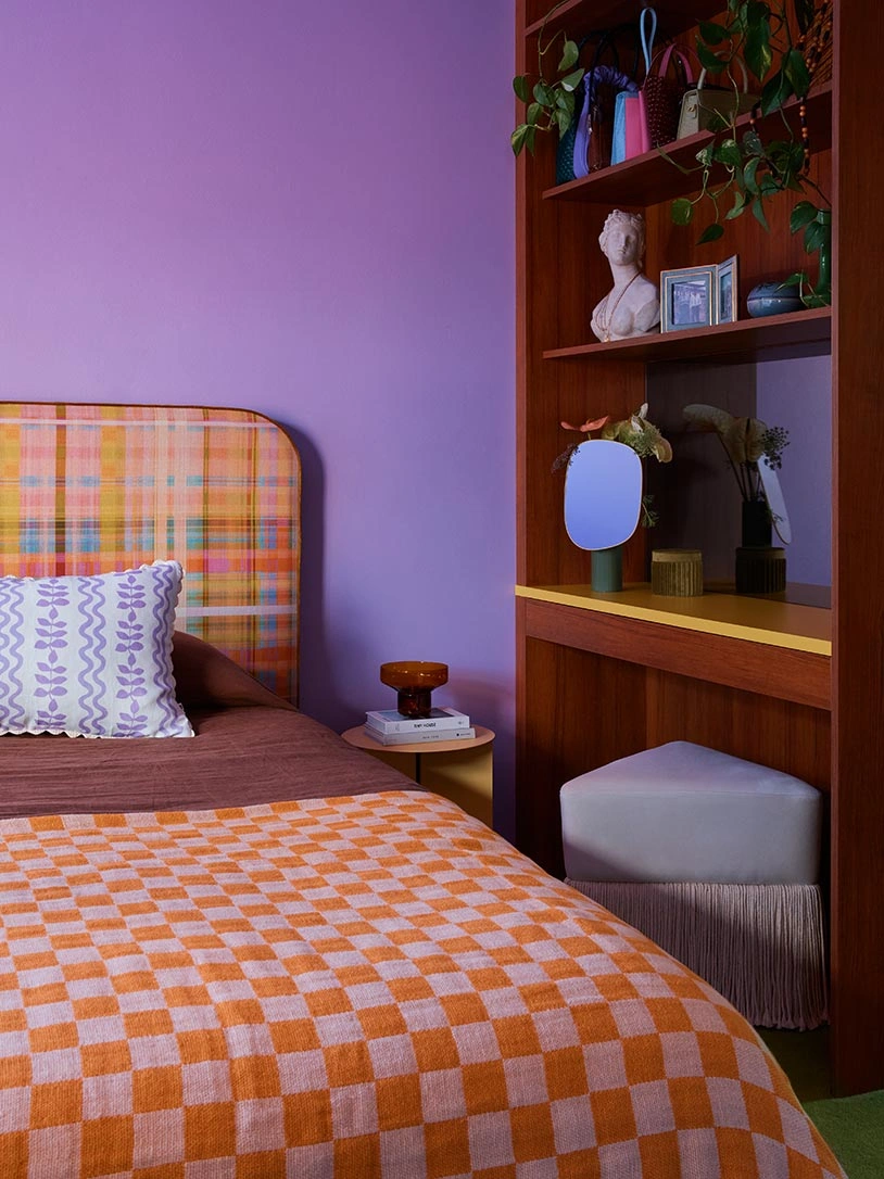 A bright bedroom showcasing purple walls and a bed covered in an orange and white checkered bedspread