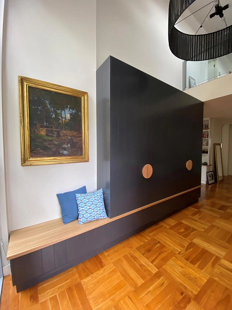 A big black wall with a simple bench and an eye-catching painting, blending modern art with functional seating