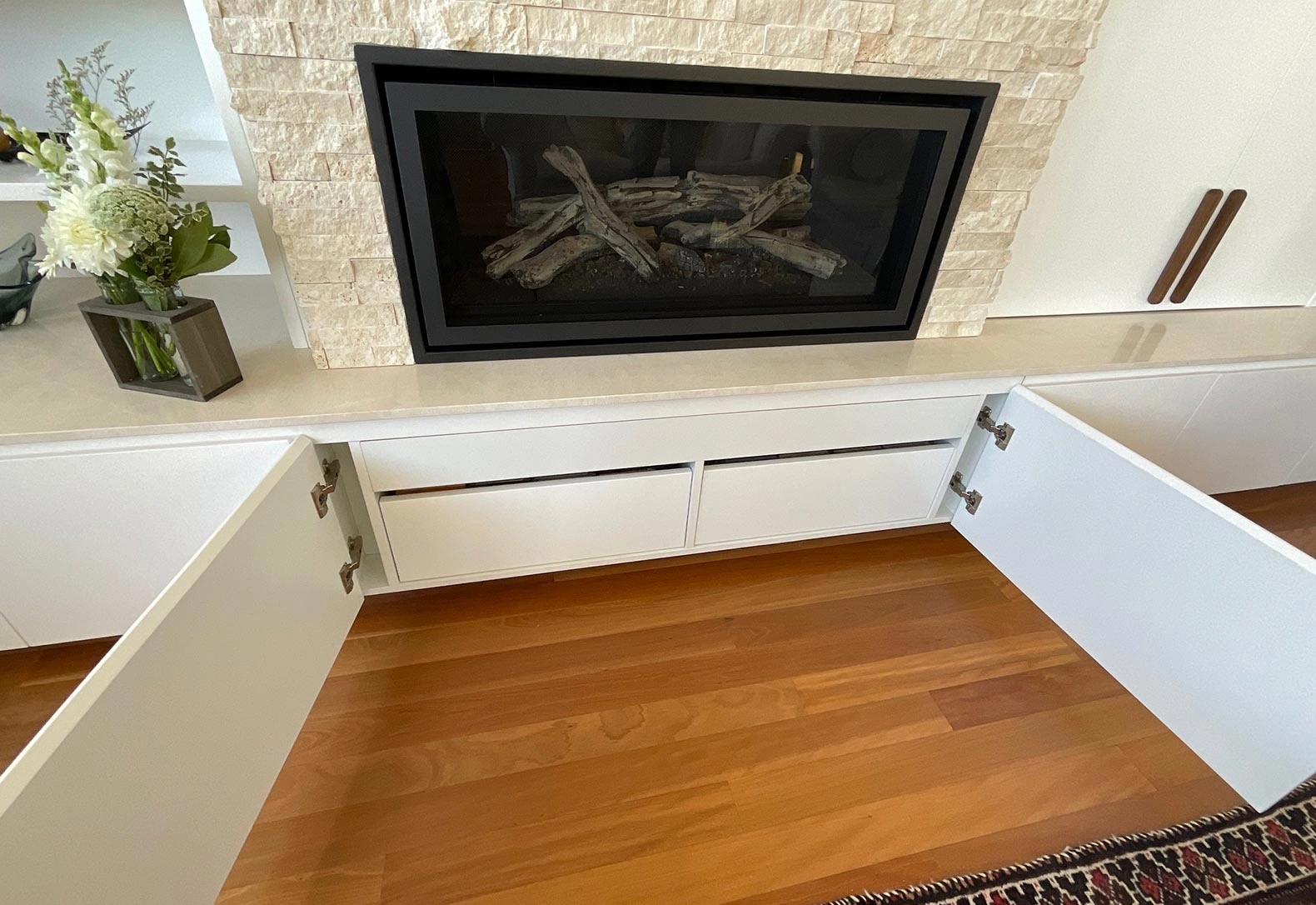 A modern fireplace with a built-in cabinet, set against a backdrop of a decorative rug on the floor