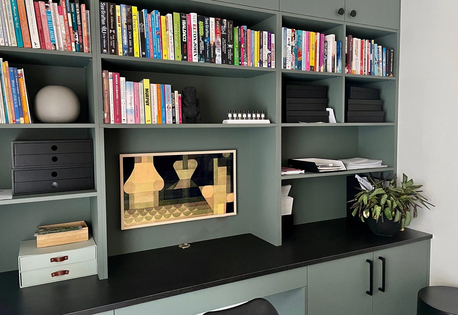 A well-organized home office featuring a wooden desk and a tall bookshelf filled with books and decorative items