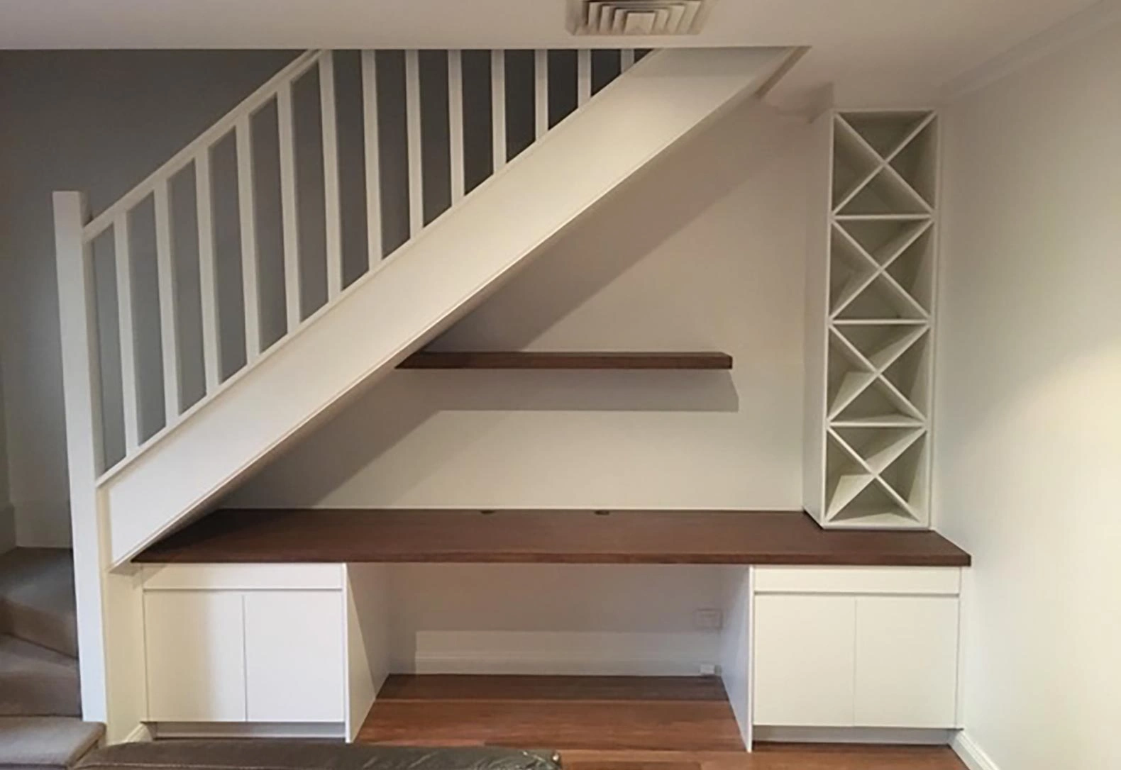 A white desk positioned under a staircase, complemented by a shelf for added storage and organization