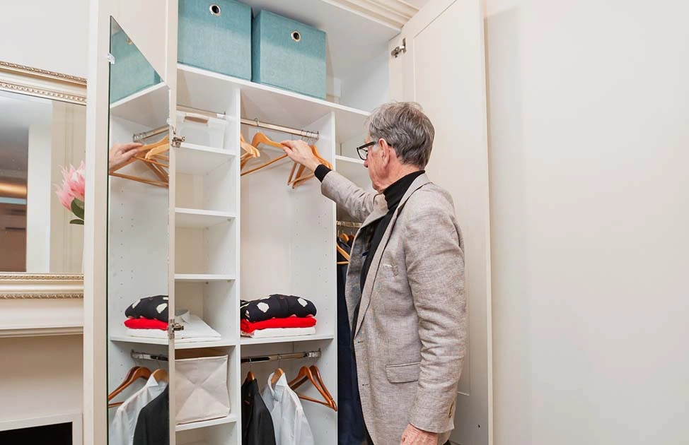 A man is arranging clothes inside a closet, ensuring everything is in its place