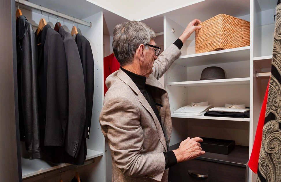 A man stands in front of a closet, browsing through different clothes and deciding what to wear