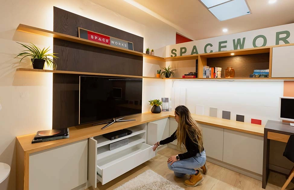 A woman carefully places a TV on a shelf in a cozy room, focusing on her task with determination