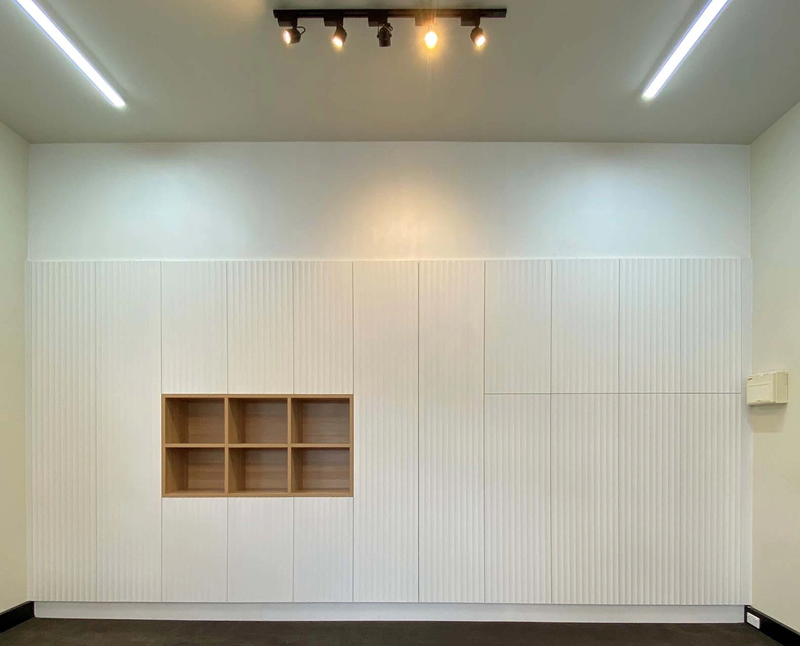 A clean white room with a wooden shelf against the wall and a modern light fixture