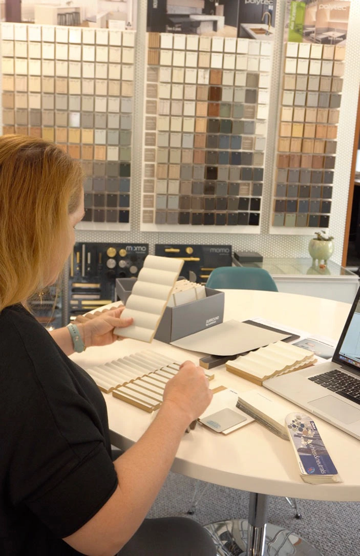 A woman sits at a table, focused on her laptop, with a box of colorful tiles beside her