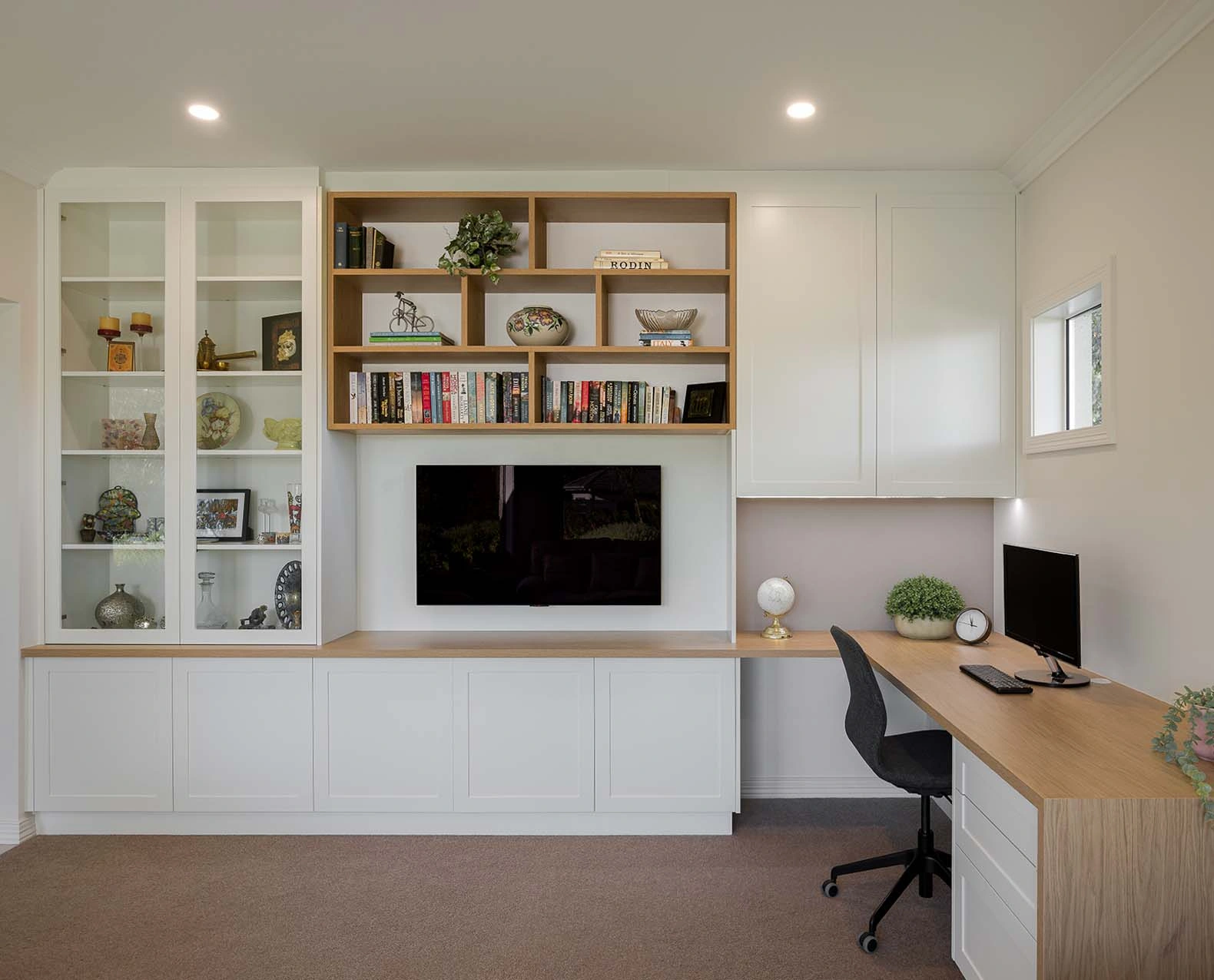 A well-organized home office featuring a desk, a bookshelf filled with books, and a television for entertainment